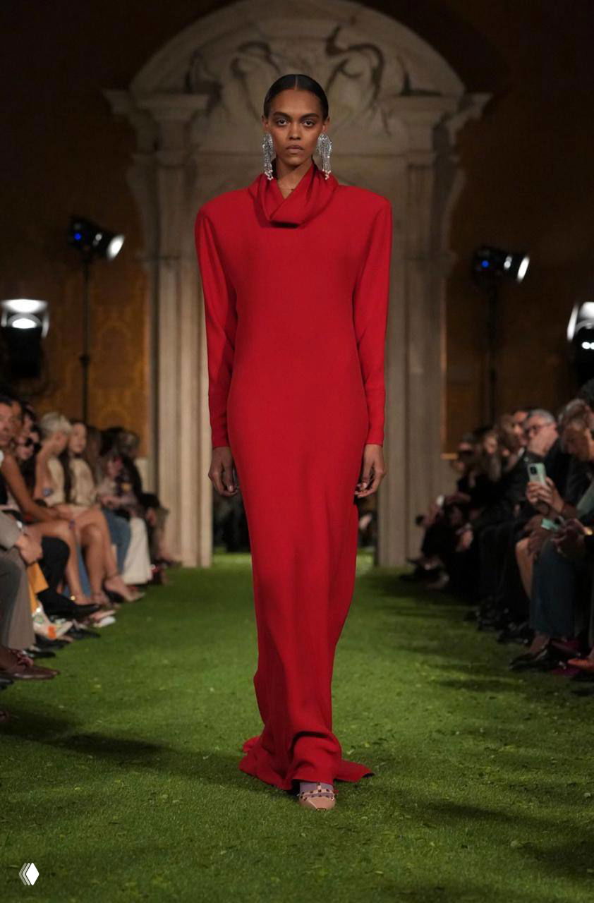 Модель в длинном красном платье и выразительными серьгами проходит по подиуму на показе Valentino, организованном в Риме.