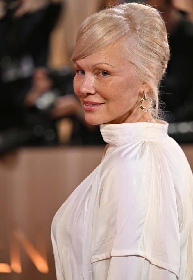 Крупный план женщины с жемчужным платиновым оттенком волос, естественным макияжем и мягкими чертами лица на фоне мероприятия.