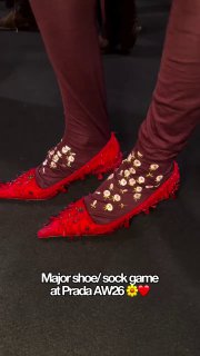 Крупный план с показа Prada AW26: ярко-красные туфли на фигурном каблуке в сочетании с украшенными носками — стилистический акцент подиума.