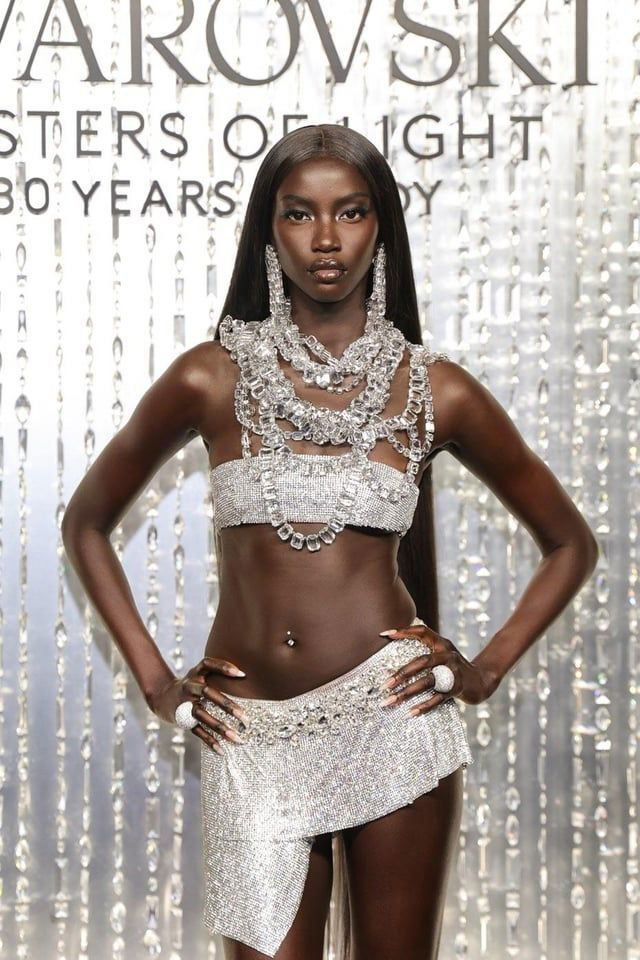 Анок Яй на подиуме в сверкающем серебристом образе: полный рост модели в украшениях и кристаллическом декоре на фоне бренда