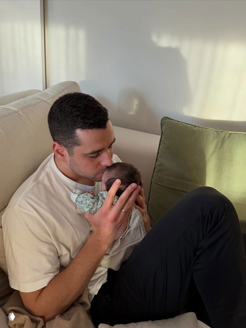 Муж Бланки Падильи бережно держит и целует новорождённую дочь Майлу — нежный момент отца и ребёнка в домашней атмосфере.