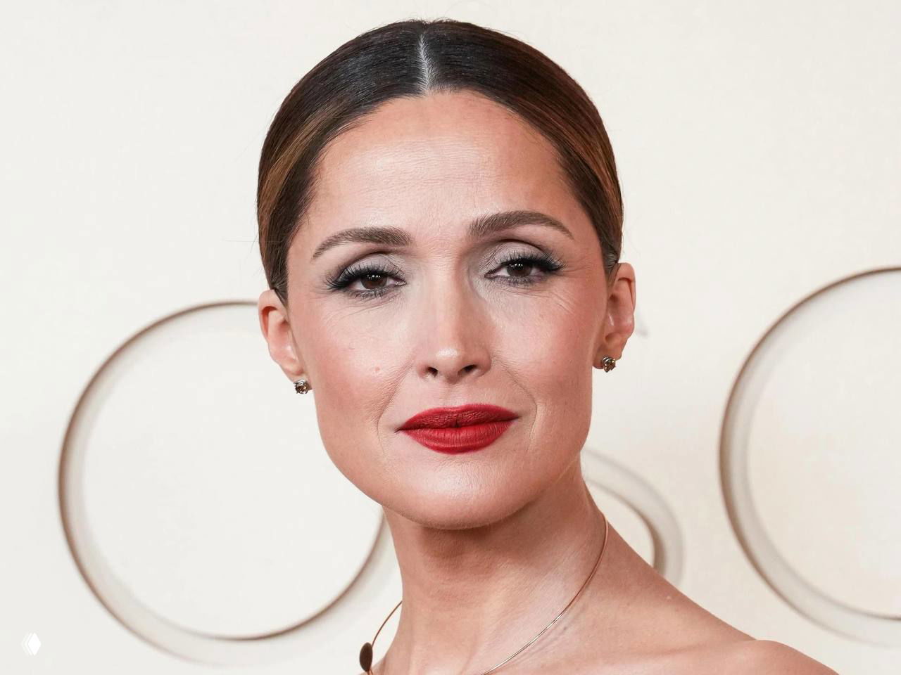 Крупный план женщины с алой помадой на нейтральном фоне «Оскар», акцент на губах и лёгкая дымка на веках.