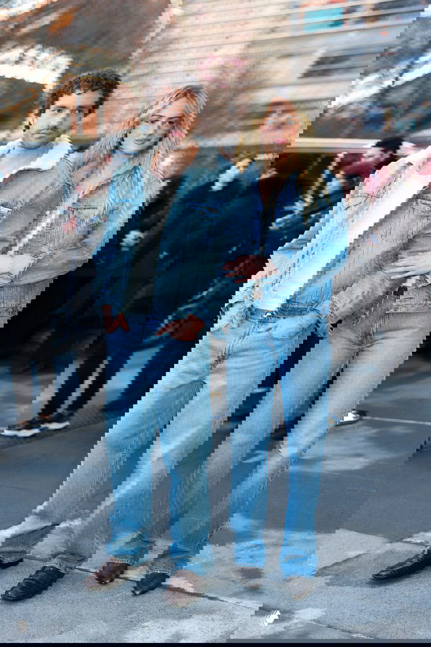 Парная уличная фотография: мужчина и женщина в джинсовых сочетаниях стоят вместе перед входом на показ на асфальтовом фоне.