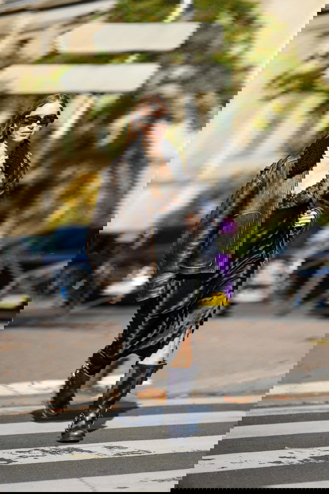 Модель на улице в чёрной шелковой комбинации и коричневой кожаной куртке, образ с грубыми ботинками и солнцезащитными очками.