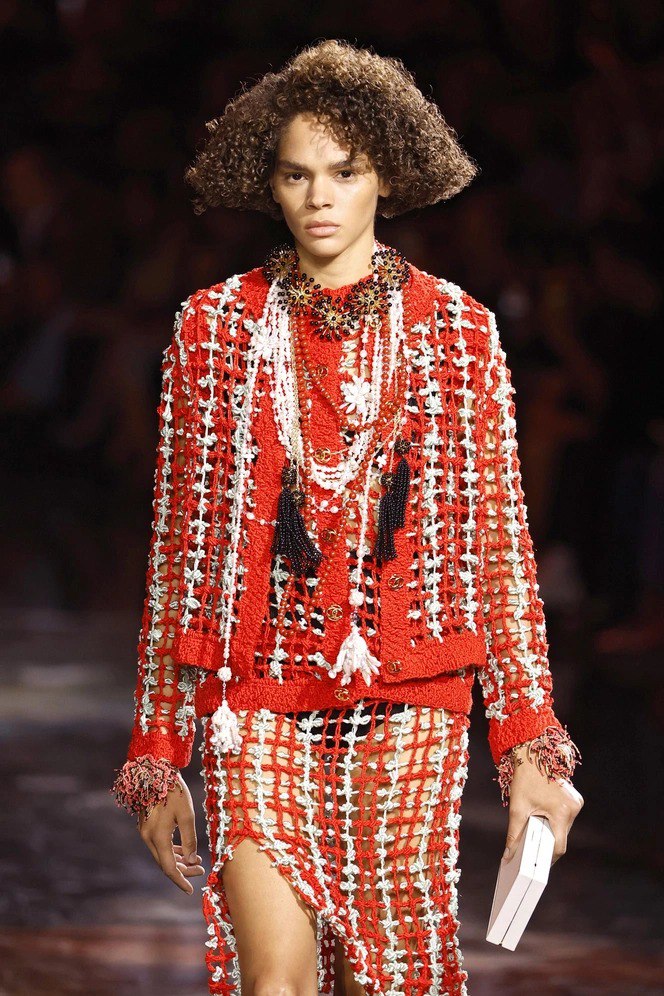 Подиумный снимок: модель в текстурированном красном комплекте и контрастной помаде, кадр демонстрирует ретро‑элементы и выразительный губной акцент на шоу