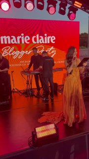 Сцена Blogger Party: ведущая в оранжевом платье на фоне большого красного экрана с логотипом Marie Claire во время мероприятия.