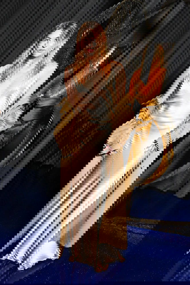 Девушка в кремовой шелковой комбинации и тренче позирует у декорации, образ сочетает нежную ткань и классический верх.