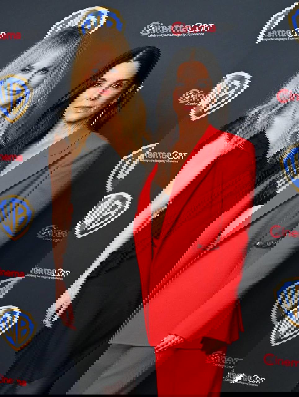 Две женщины в вечерних нарядах позируют вместе на фоне логотипов Warner Bros и CinemaCon, официальный фотоколл с элегантными образами и светом для прессы.