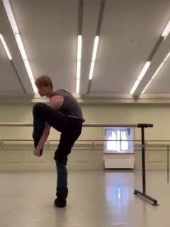 Кадр из репетиционного зала: мужчина в движении возле станка в спортивной одежде, подготовка балетного номера или тренировки.