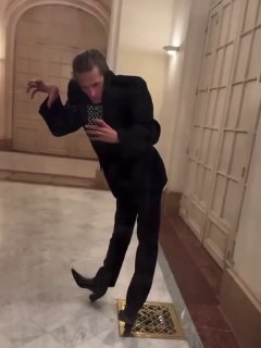 Кадр из короткого видео: мужчина в темном костюме в декоративном зале делает театральный жест, кадр в движении для соцсетей.