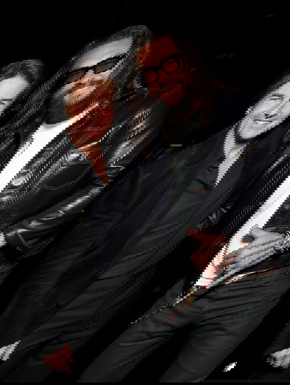 Два актёра в кожаных и тёмных образах улыбаются на фоне чёрной сцены, видны аксессуары и татуировки, неформальный и дружелюбный кадр с мероприятия.