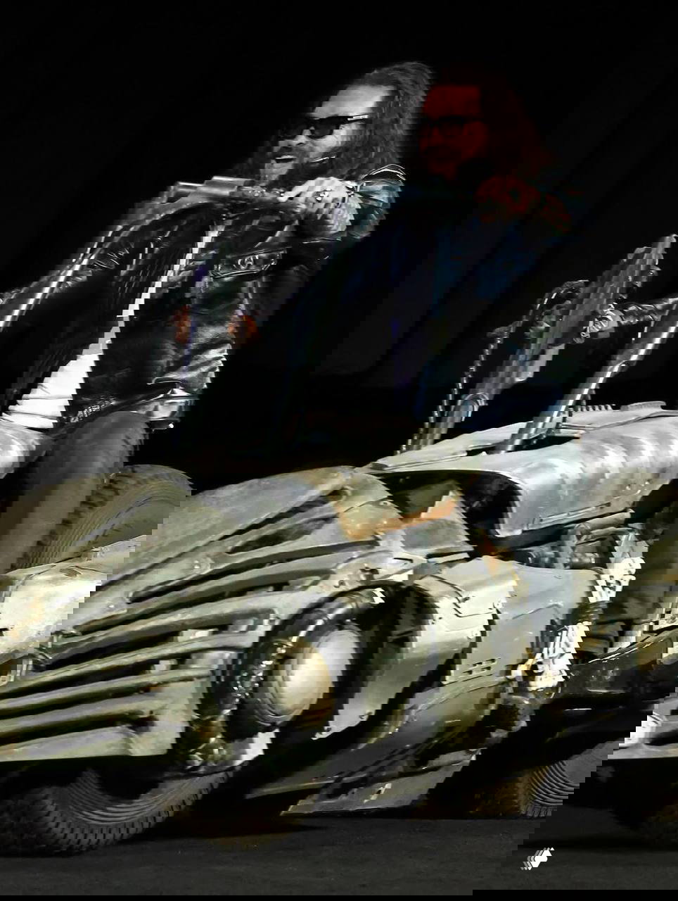 Человек в кожаном пиджаке сидит на крупном эффектном сценическом байке с футуристическим дизайном, демонстрация реквизита фильма прямо на сцене CinemaCon.