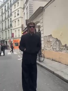 Уличный кадр в Париже: мужчина в длинном темном пальто идет по улице, городской фон и архитектура на заднем плане.