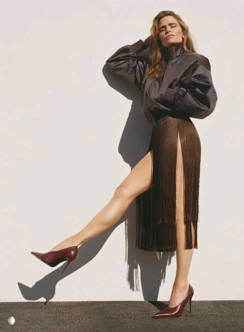 Фотография с удлиненной тенью: женщина в юбке с бахромой и туфлях на каблуке, акцент на ногах и динамичной позе.
