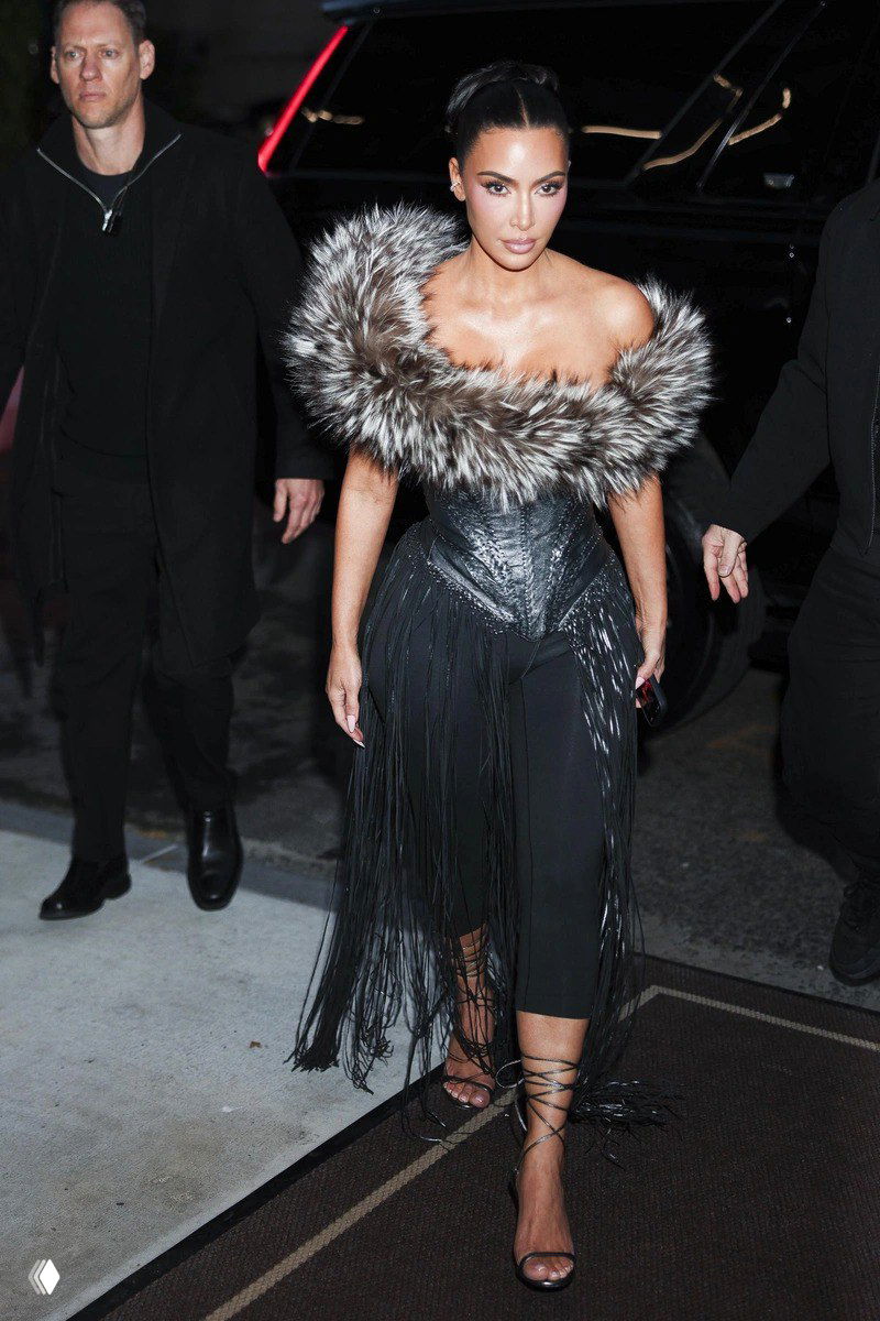 Ким Кардашьян в черном ансамбле с меховой оторочкой и бахромой, кадр с выхода — образ в сочетании корсета и узких брюк.