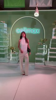 Женщина позирует в фирменной фотозоне Celimax: зелёный фон с неоновым логотипом, прозрачные декоры и лаконичная лаунж-зона.