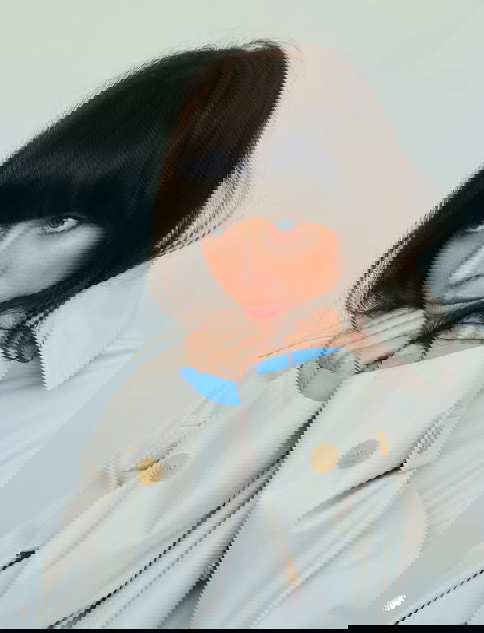 Крупный план актрисы в светлом тренче, сложенные руки у подбородка; мягкое выражение лица и акцент на текстиле верхней одежды.