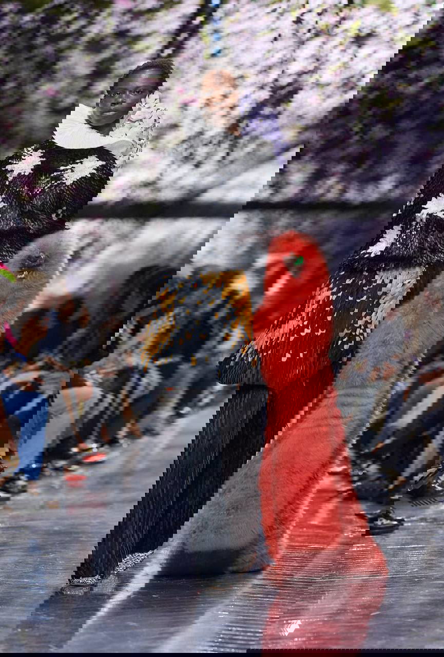 Модель в комбинированном образе с крупной оранжевой фактурной сумкой и цветочными деталями; кутюрная эстетика коллекции Dior, вдохновлённой природой.