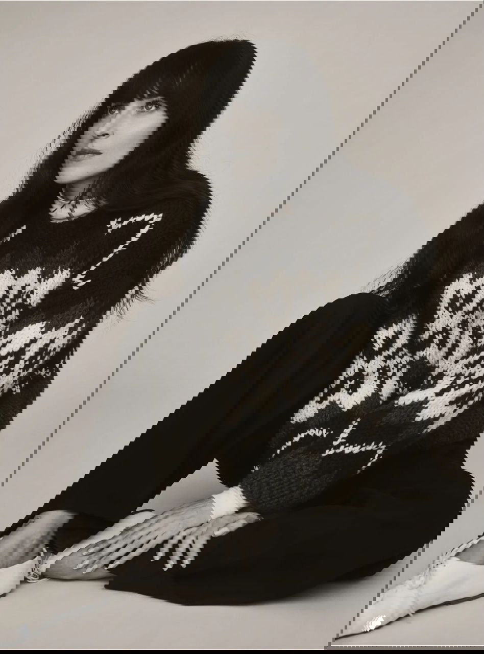 Чёрно‑белый студийный кадр актрисы в тёплом вязаном свитере и тёмных брюках; расслабленная поза и естественная мимика.