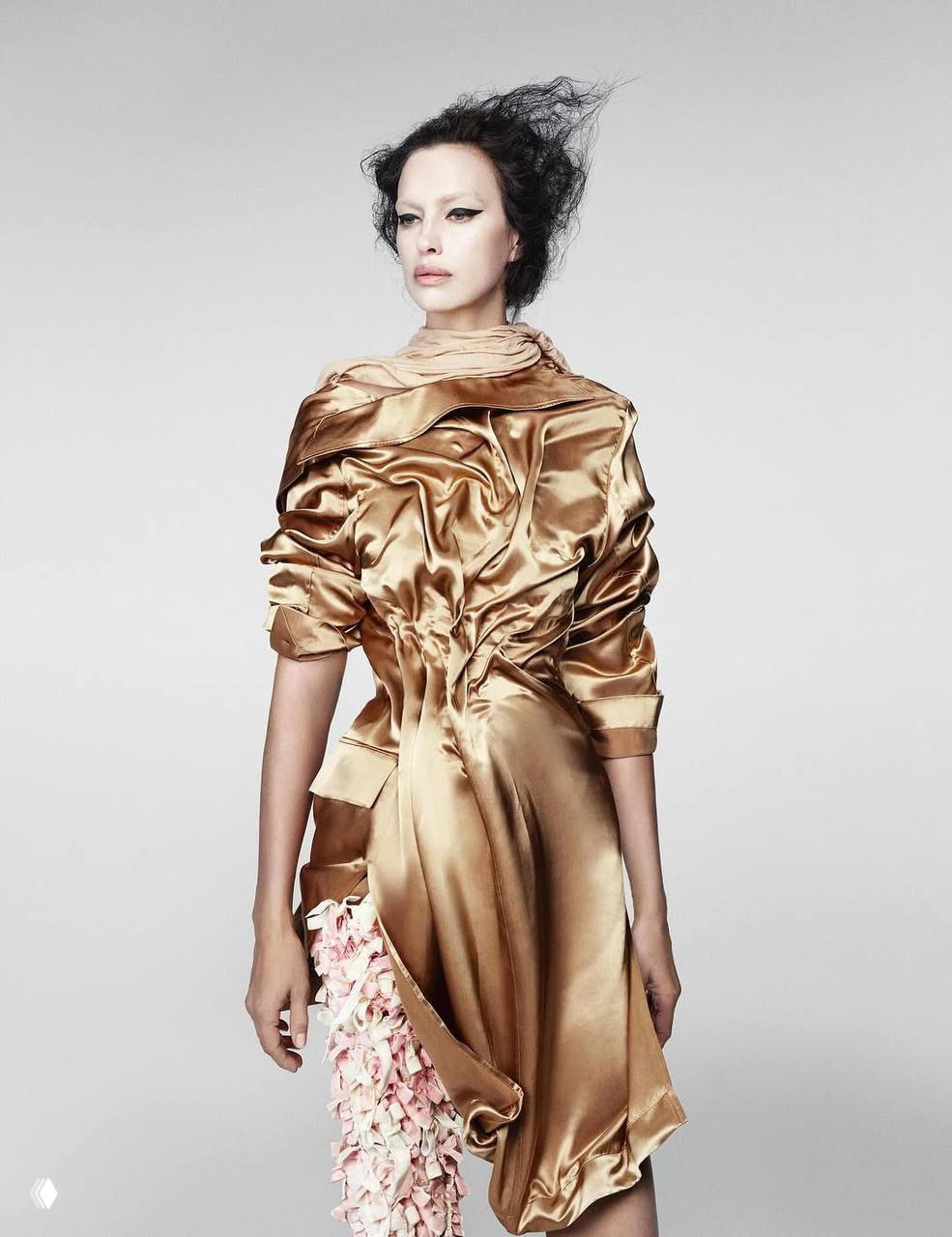 Ирина Шейк в золотистом платье с драпировками и цветочной деталью, высокий рост на монохромном фоне, минималистичная студийная постановка.