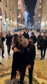 Кадр сзади: Джордж помогает Амаль при ходьбе по мраморному полу Милана, шпильки вызывают трудности при выходе.