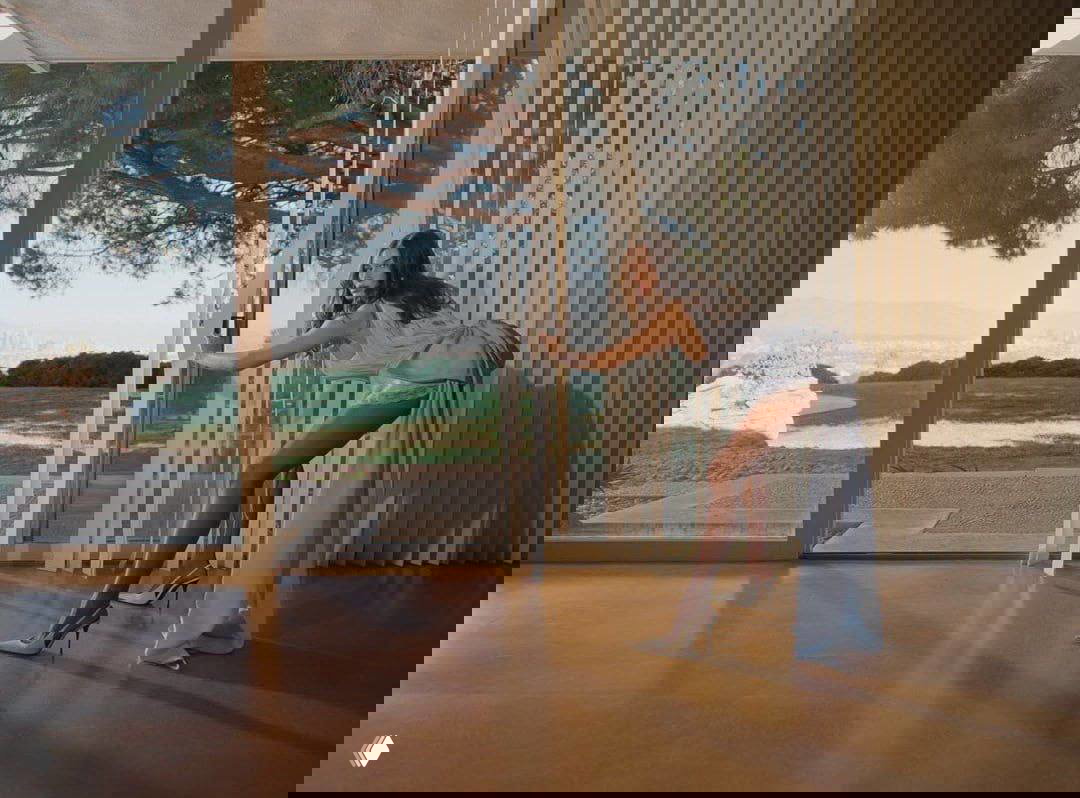 Модель у панорамного окна в длинном платье: интерьер с видом на сад за стеклом, кинематографичный свет и поза, подчёркивающая элегантность образа.