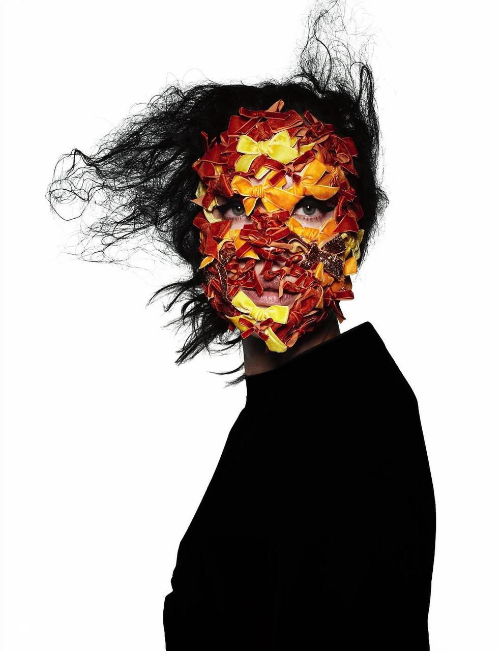 Портрет Ирины Шейк в маске из разноцветных лоскутов и текстур, драматичная причёска и контрастный свет в художественной fashion‑съёмке.