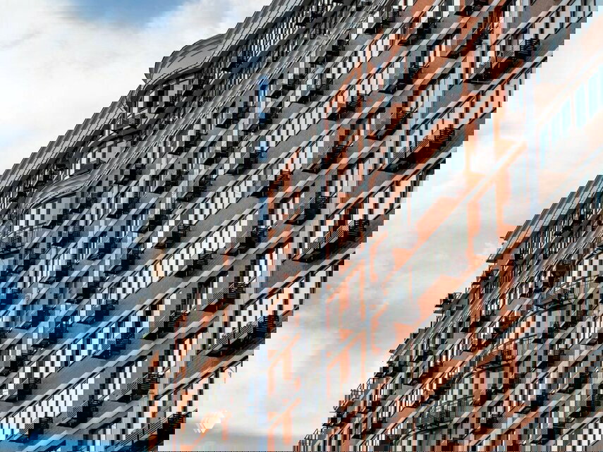 Крупный план фасада жилого дома: кирпичная отделка, вертикальные панорамные окна, небольшие балконы и архитектурные декоративные элементы на фасаде.