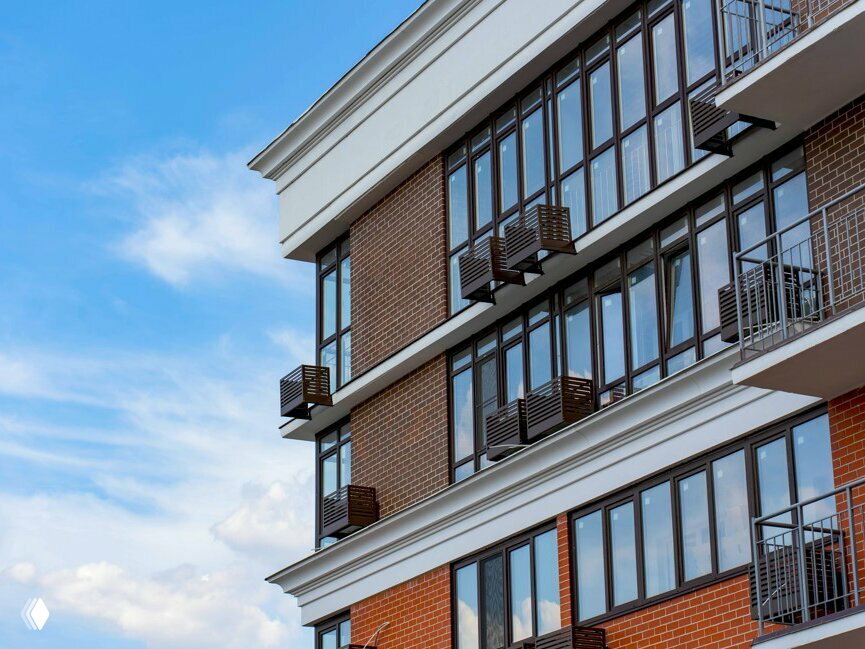 Угловой фрагмент здания с современными панорамными окнами и элементами отделки на фоне голубого неба — акцент на архитектурные решения комплекса.