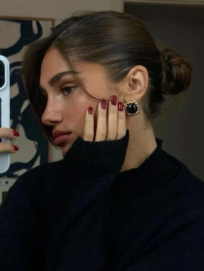 Портрет женщины, держащей подборку ногтей с насыщенно‑красным лаком: короткая форма и глянцевый финиш на примере образа.