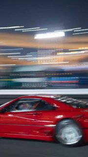 Размытое ночное фото: красный спортивный автомобиль Ferrari F40 мчится по освещённой токийской улице, создавая эффект дрифта и скорости.