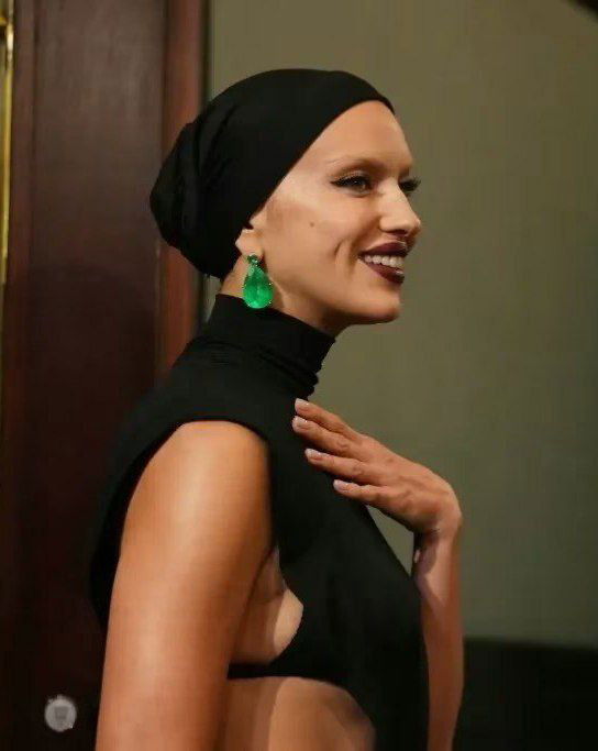 Портретный кадр сбоку: готический стиль с тюрбаном, открытым плечом, зелёными серьгами и тёмной помадой, лицо в профиль.