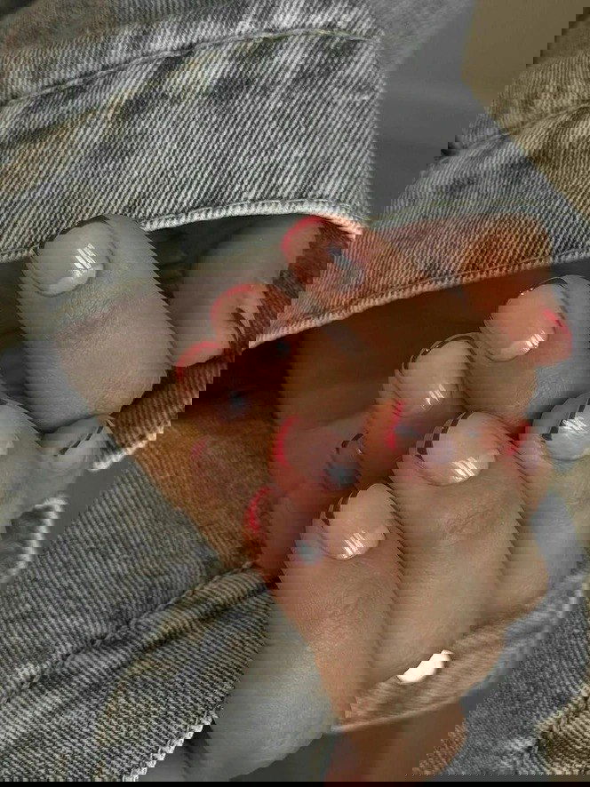 Руки в джинсовой куртке показывают маникюр с тонкой красной линией-френч по краю ногтей на светлом нейтральном фоне.