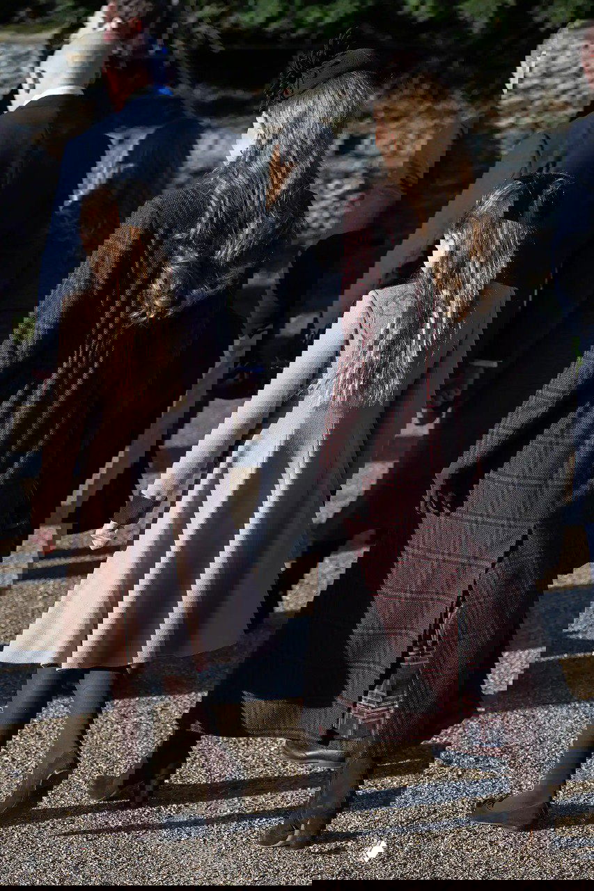 Вид сзади: женщина в тёмном клетчатом пальто и девочка в светлом пальто идут по дорожке у церкви в рождественский день.