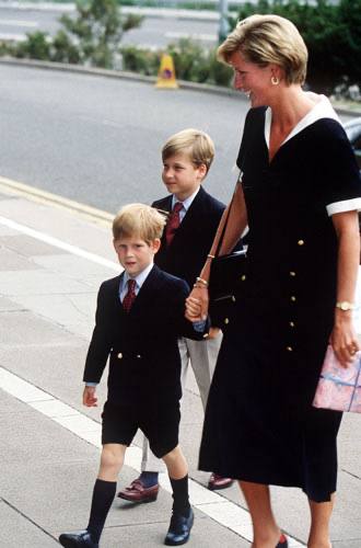 Городская сцена: женщина в строгом чёрном платье идёт рядом с двумя детьми, повседневный семейный образ на улице.