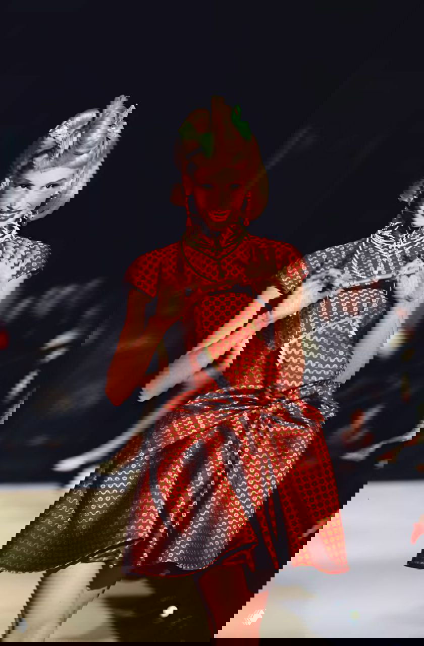 Модель в красном шелковом платье с крупным бантом и жемчужными ожерельями на подиуме Dior осень‑зима 1997, ретро‑гламур, акцент на аксессуарах.