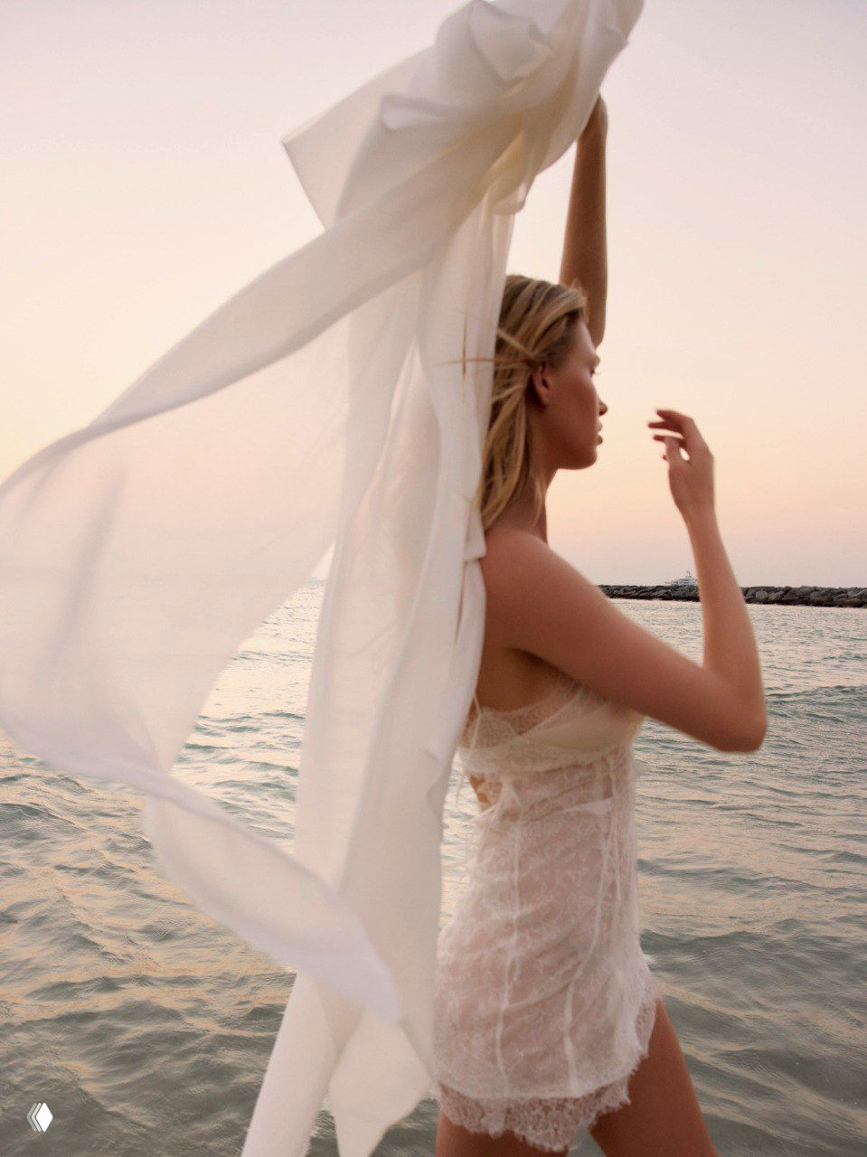 Модель на пляже в лёгком полупрозрачном платье, развевающаяся ткань и морской горизонт создают атмосферу свободы и летней нежности.