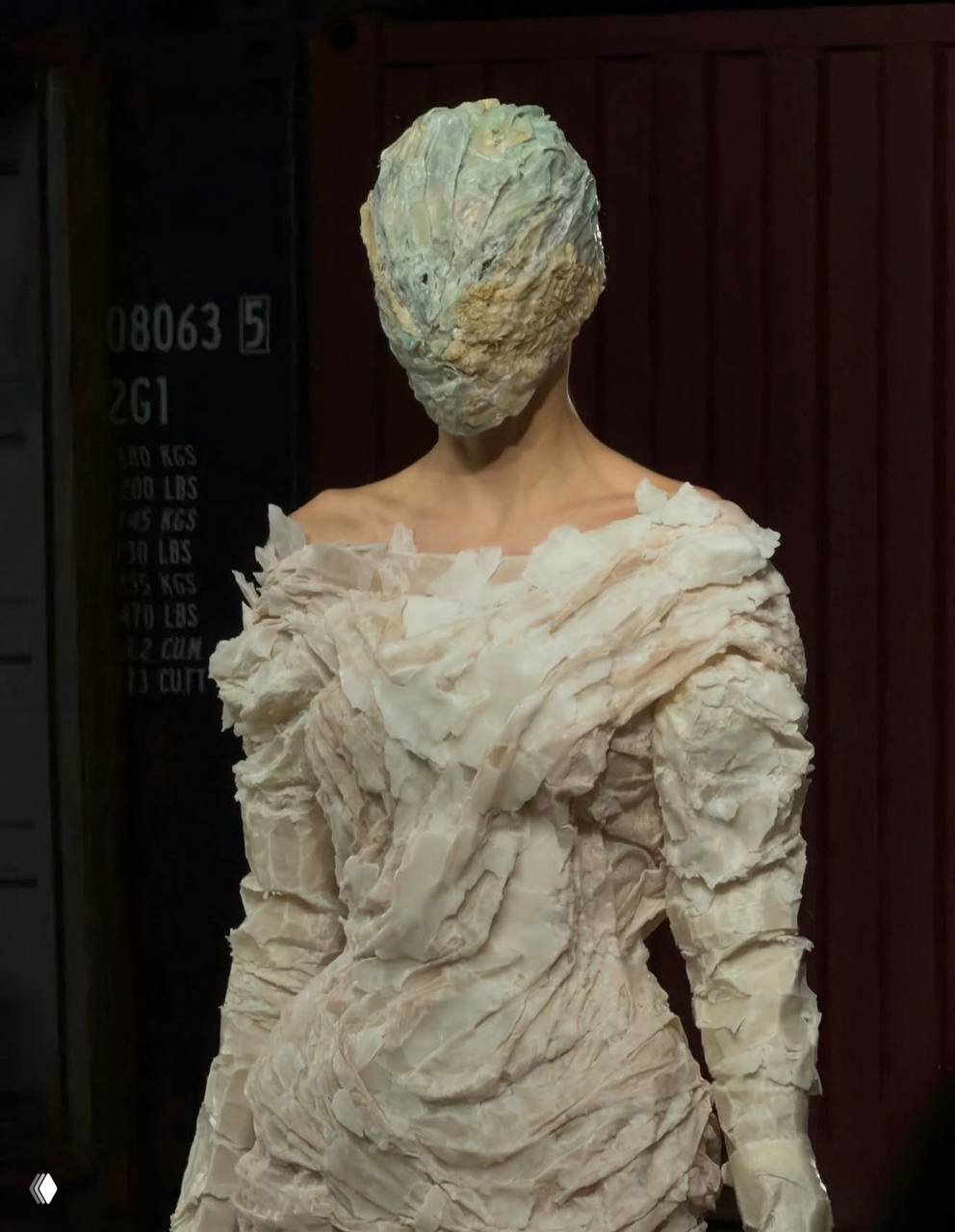 Модель в светлом платье с фактурной обработкой и полностью закрытой маской, силуэт напоминает фарфоровую статуэтку в эстетике Artisanal.