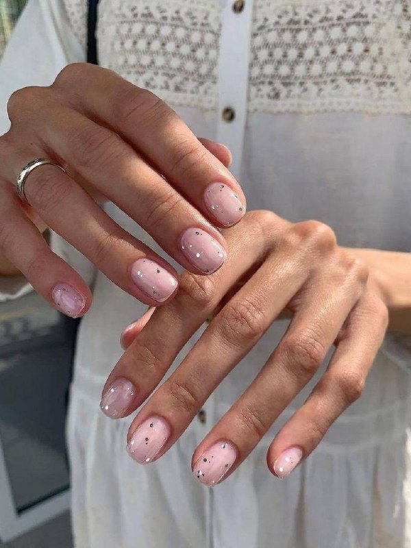 Руки в светлой рубашке с короткими овальными ногтями бледно-розового цвета и небольшим блеском — форма подчеркивает вертикаль и стройность пальцев.