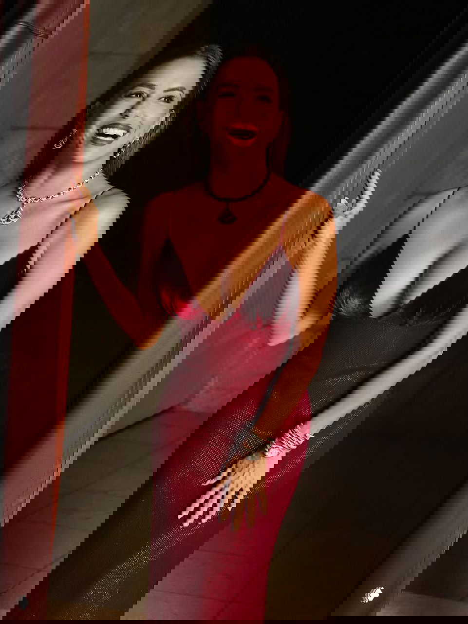 Крупный план женщины в красном платье в украшениях Bvlgari, смеётся на фоне тёмной сцены; акцент на декольте и ювелирном комплекте.