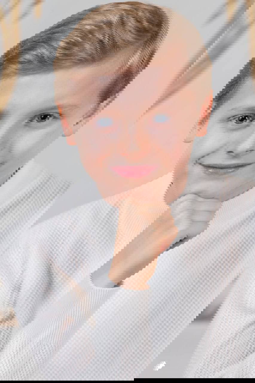 Официальный портрет принца Монако Жака, 11 лет: портрет крупным планом в белом свитере, лёгкая улыбка и нейтральный интерьер официальной фотосессии.