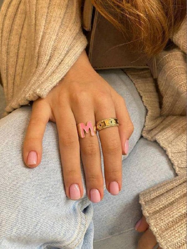 Рука с короткими полукруглыми ногтями розового оттенка и кольцами на пальцах — форма аккуратно удлиняет средние пальцы, фото в интерьере.