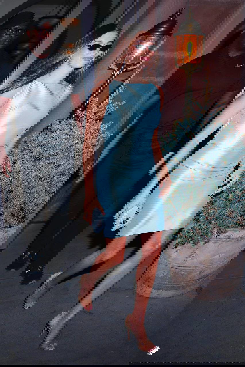 Женщина в нежно-голубом облегающем платье идёт по улицам, образ выглядит как вечерний выход в лаконичном минималистичном стиле.