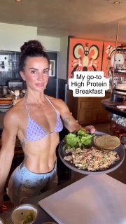 Сенада держит большую тарелку высокобелкового завтрака на кухне; на кадре видна подпись "My go-to High Protein Breakfast".