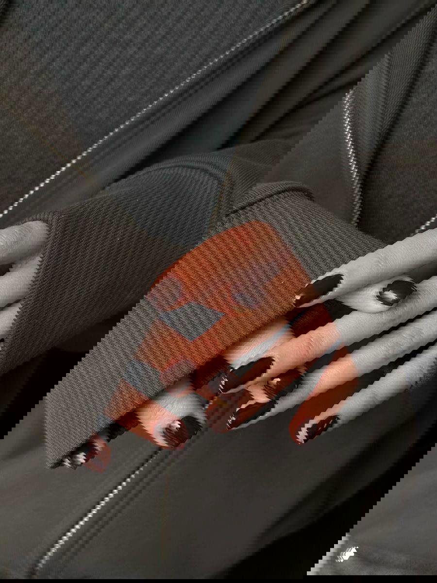 Руки в тёмной одежде с квадратными ногтями средней длины тёмно-шоколадного оттенка — квадратная форма добавляет статичности и подходит для длинных тонких пальцев.