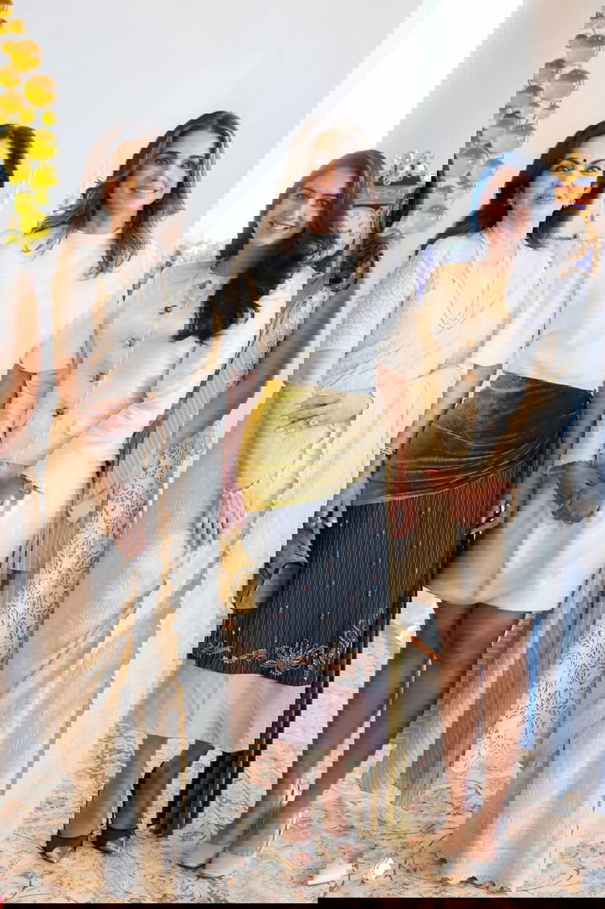 Группа женщин в торжественной обстановке: слева традиционный сари, в центре женщина в белом топе с бархатным акцентом на юбке, справа светлый костюм — общий портрет на мероприятии.