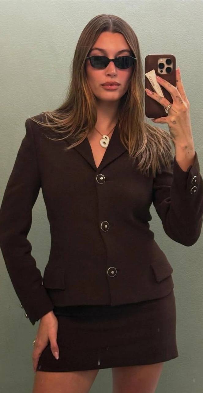 Крупный план: женщина в солнцезащитных очках и светлом наряде держит верёвку на сцене, поза подчёркивает стройность и вечерний образ.