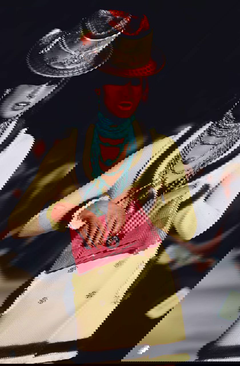 Модель в светлом жакете с бирюзовыми ожерельями и розовой сумкой на подиуме Dior осень‑зима 1997, акцент на аксессуарах и текстуре ткани.