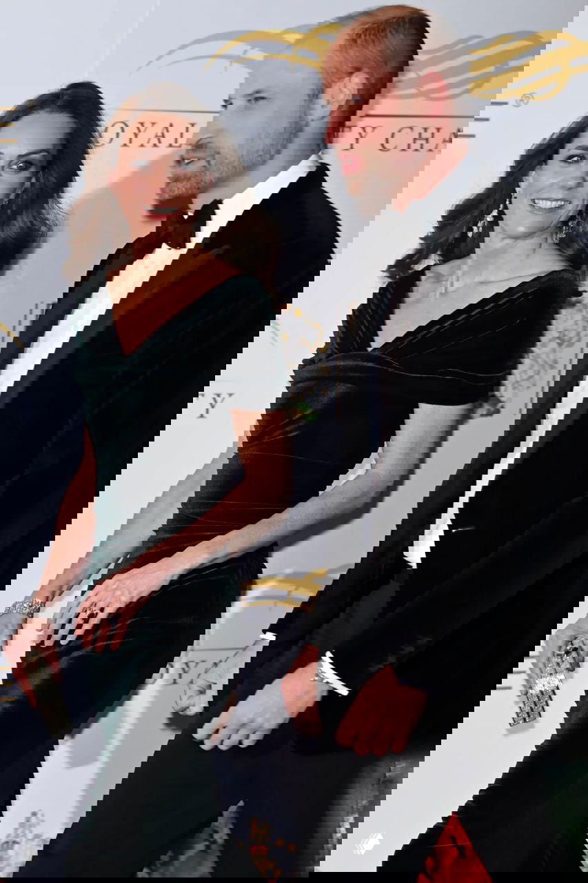 Женщина в тёмно‑зелёном платье рядом с мужчиной в чёрном смокинге на фоне баннера Royal Variety Performance.