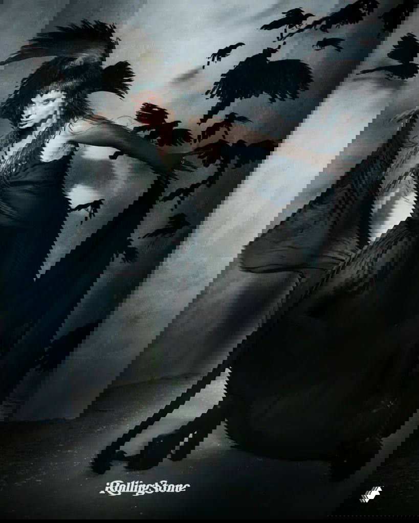 Драматичный кадр: женщина в чёрном платье с развевающейся тканью на фоне силуэтов птиц, образ в готическом стиле.